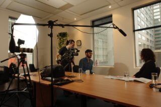 Woman sitting at a table being interviewed by a film crew