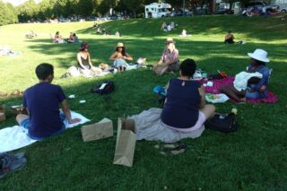 People sitting in a large circle on a grass field in a park
