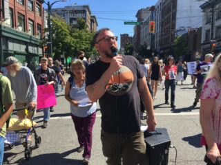 A man on a loudspeaker talking to a marching crowd as he marches with them