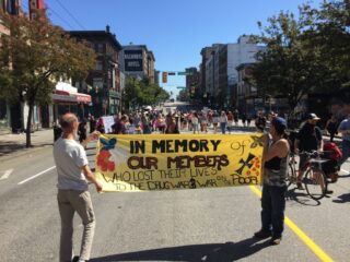 Two people carrying a yellow banner ahead of a large marching crowd in downtown Vancouver