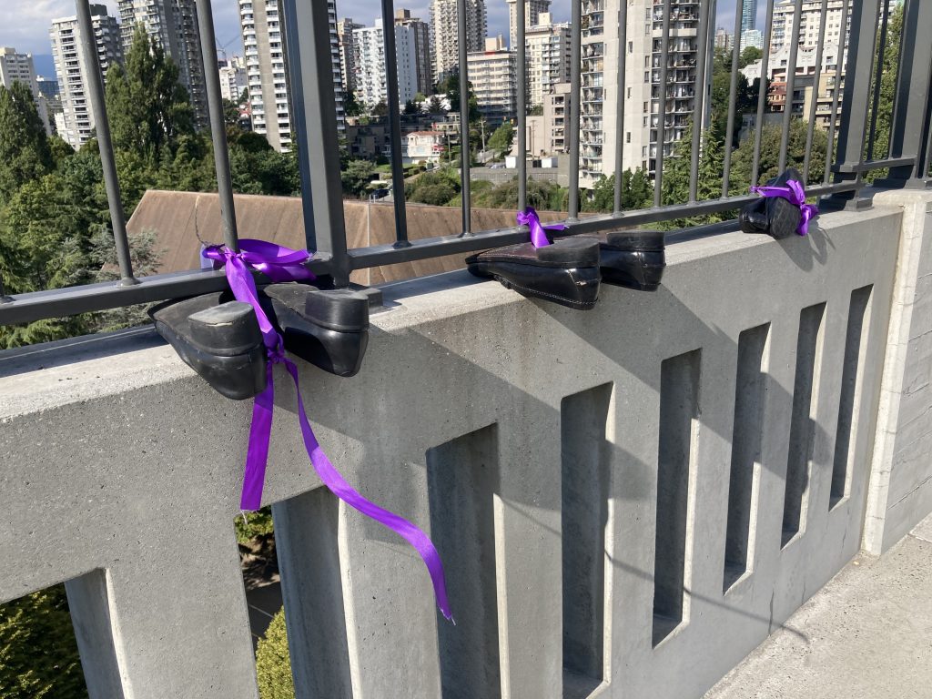 Three pairs of shoes tied with a purple ribbon to the Burrard Street Bridge