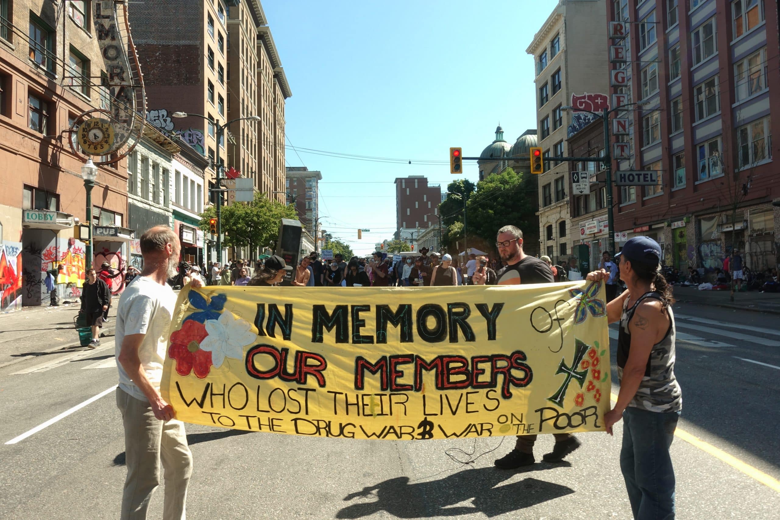 Two people carry a large banner down the street that reads "In Memory Our Members"