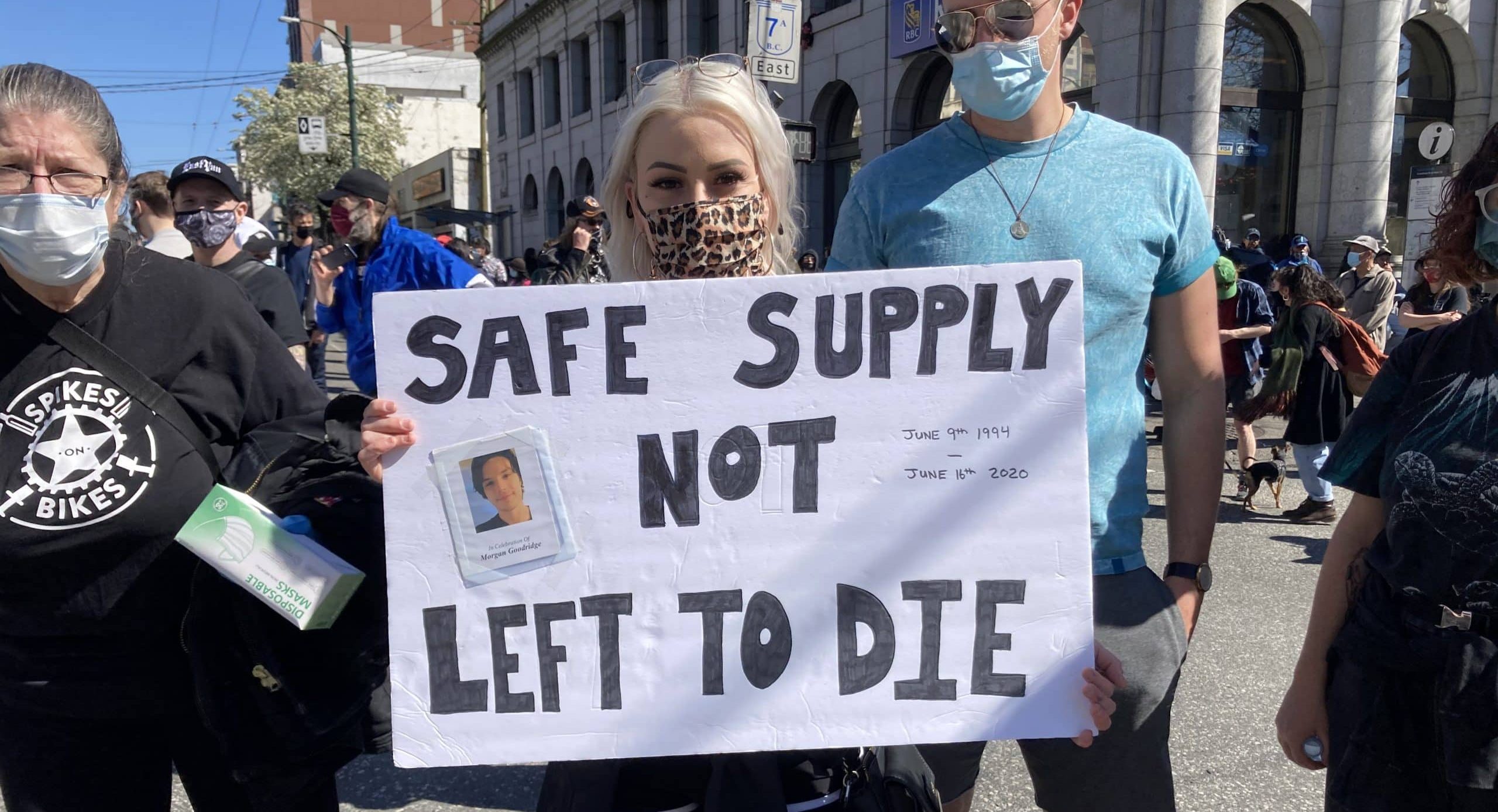 A person holding a sign reading "safe supply not left to die"