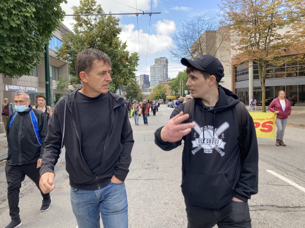 Dr. Mark Tyndall and Matt Bonn talking to each other while walking down a street