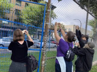 Three people tyding wooden feathers to a fence